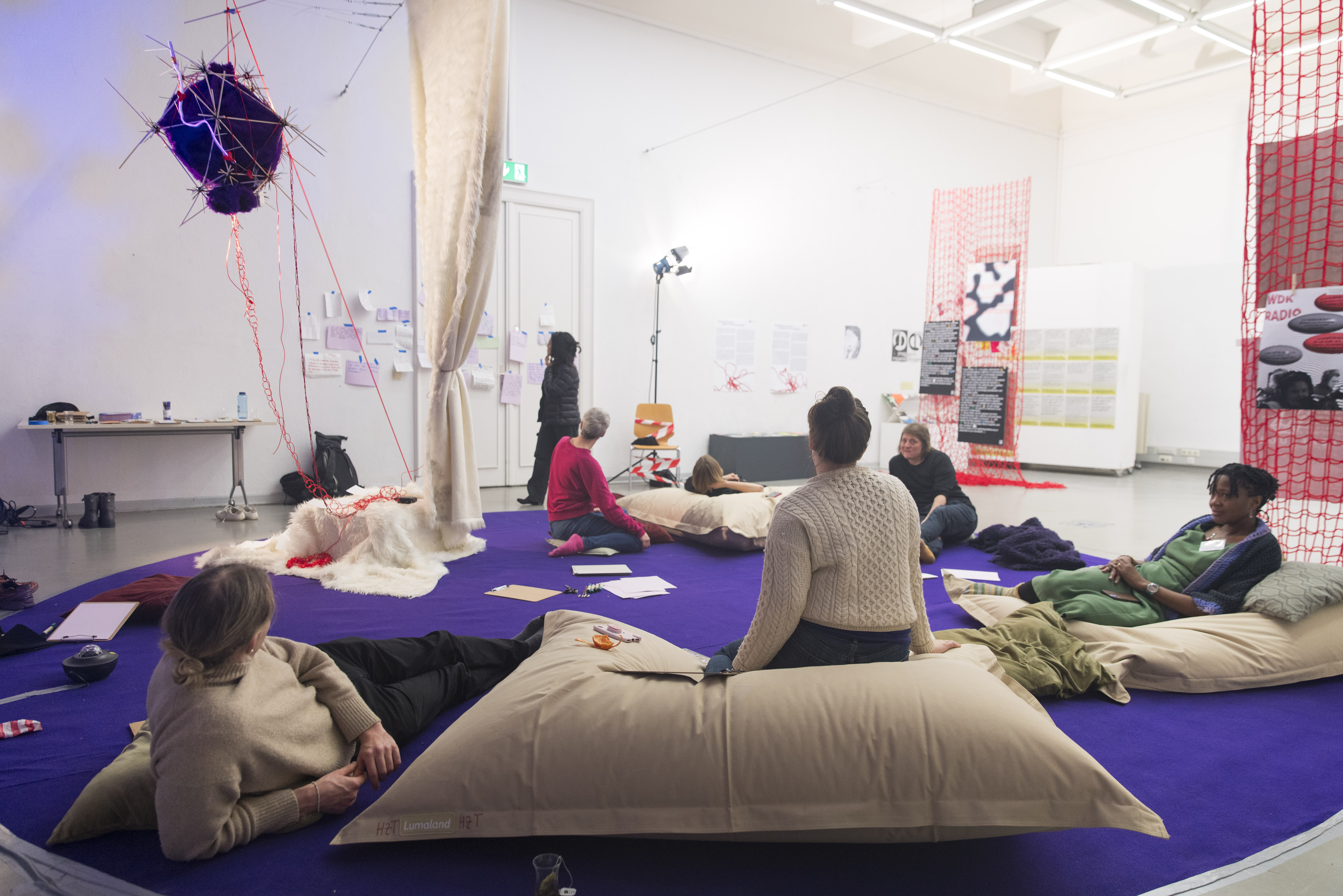 Image of a circle of people in a workshop on white pillows on a purple carpet