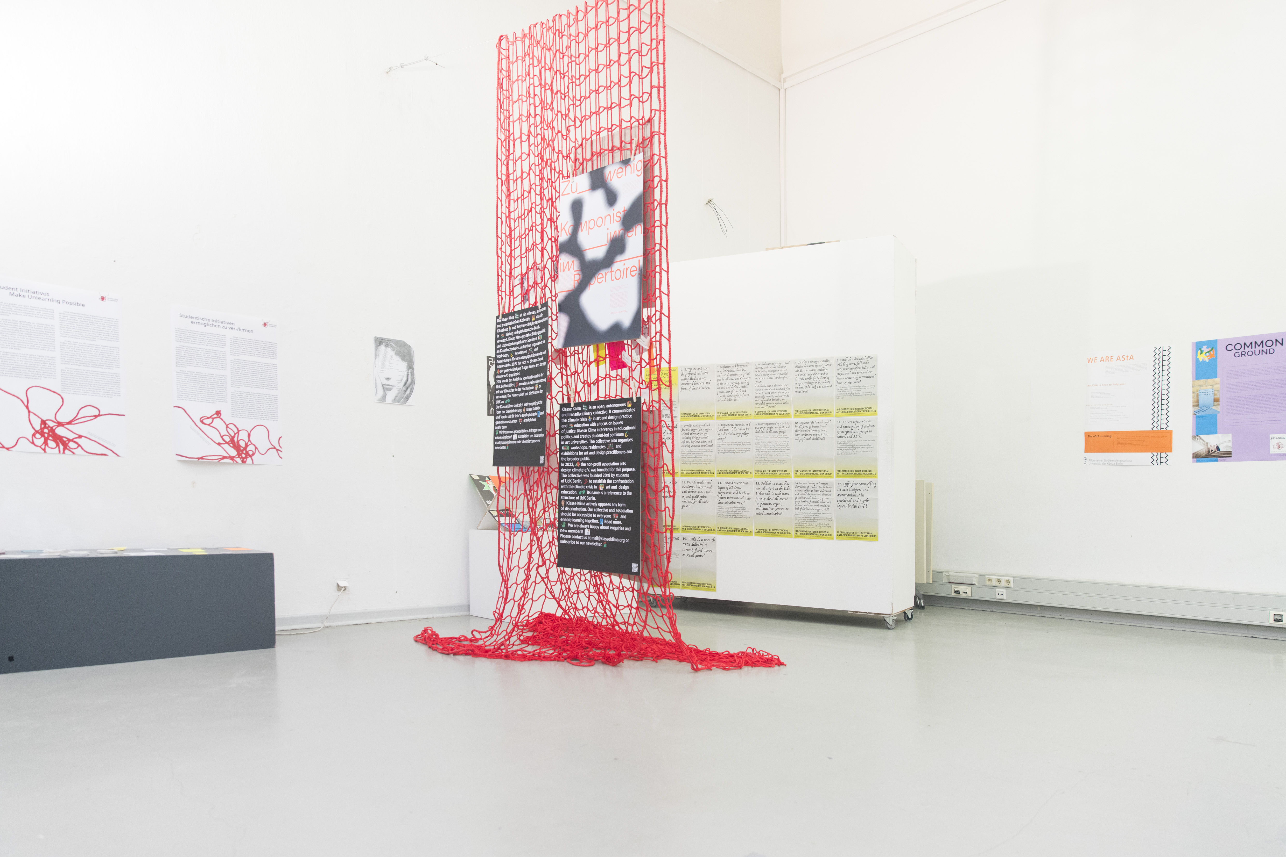 Image of an exhibition space with posters hanging from a red net and on white walls