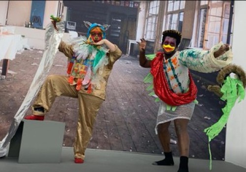 Two people in colourful costumes pose with their arms and one leg lifted high.